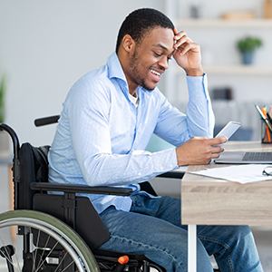 A man seated in a wheelchair smiling and reading his phone.